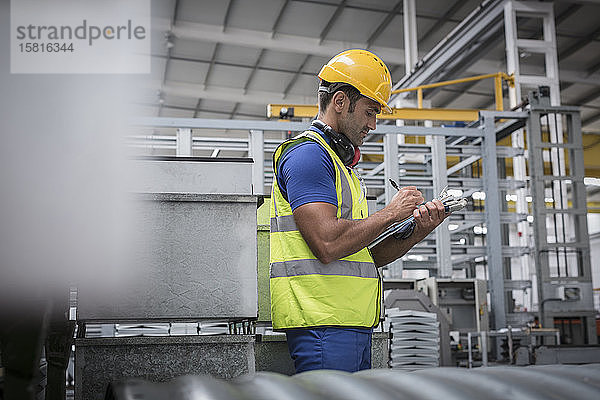 Männlicher Vorgesetzter schreibt auf einem Klemmbrett in einer Fabrik