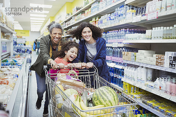 Verspielte Mehrgenerationen-Frauen  die einen Einkaufswagen im Supermarktgang schieben