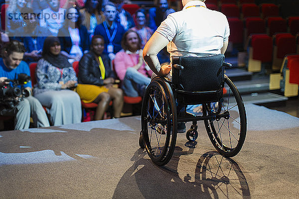 Publikum beobachtet Rednerin im Rollstuhl auf der Bühne