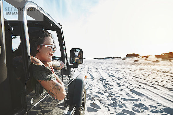 Lächelnde junge Frau lehnt sich aus dem Jeep-Fenster und genießt den Strandausflug