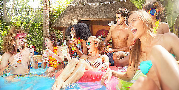 Junge Freunde lachen  hängen herum und trinken im sonnigen Sommerschwimmbad