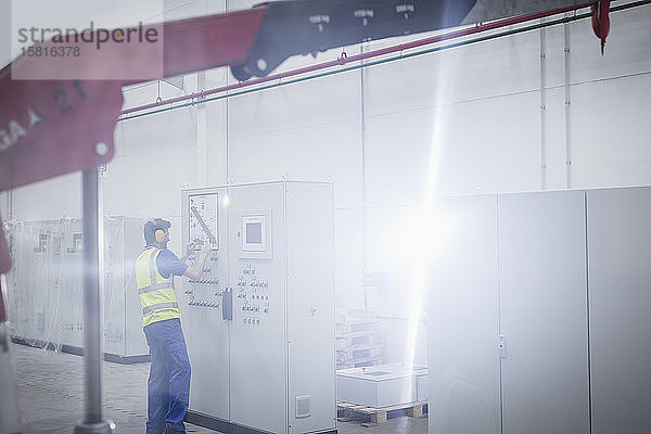 Männlicher Arbeiter  der eine Maschine am Schaltpult in einer Fabrik bedient