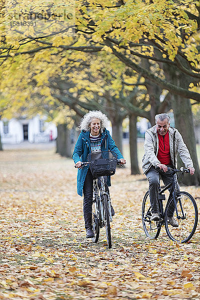 Älteres Paar fährt mit dem Fahrrad zwischen Blättern und Bäumen im herbstlichen Park