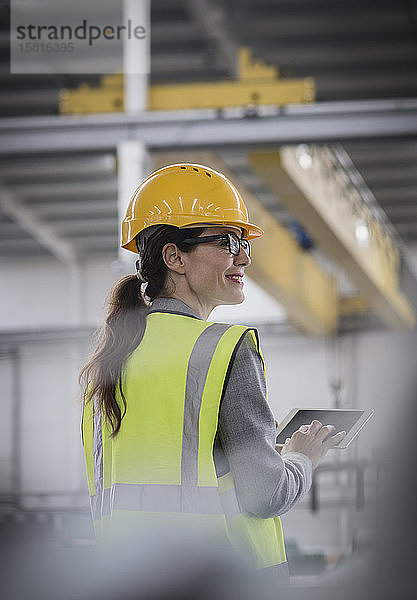 Selbstbewusste  lächelnde Arbeiterin  die in einer Fabrik ein digitales Tablet benutzt