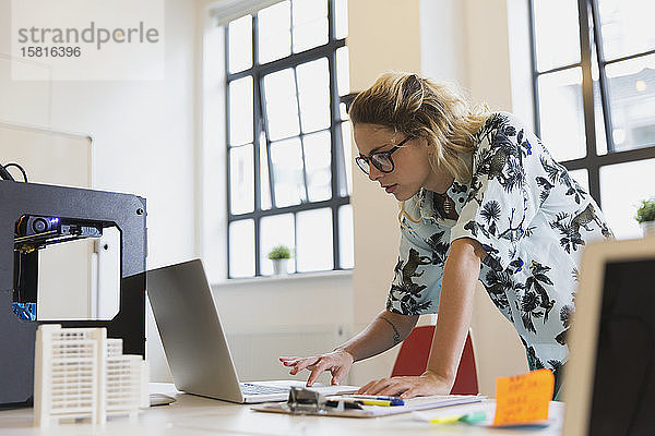 Eine Designerin arbeitet an einem Laptop neben einem 3D-Drucker im Büro