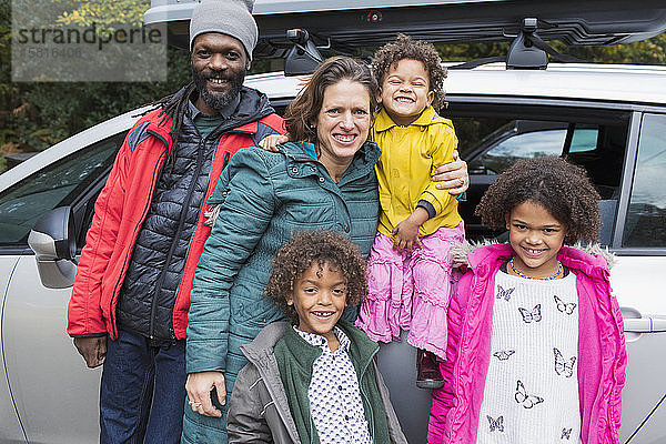 Porträt einer glücklichen Familie vor einem Auto auf einem Parkplatz