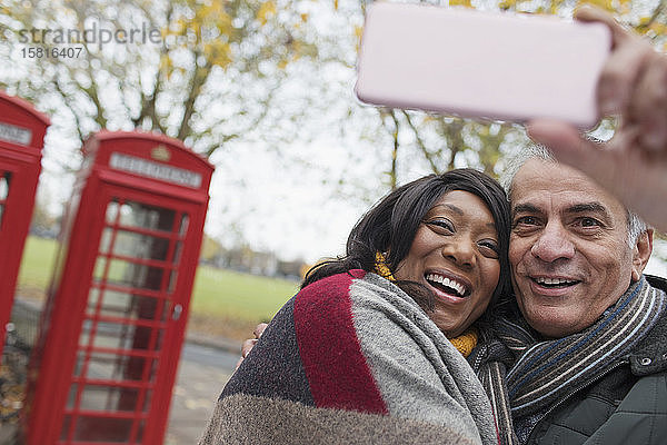 Zärtliches älteres Paar macht ein Selfie im Herbstpark vor einem roten Telefonbuch