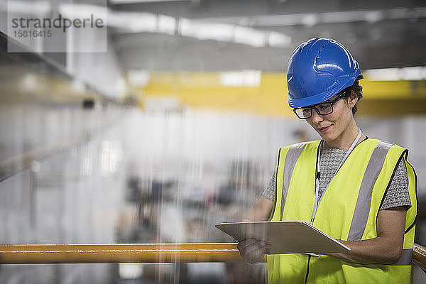 Weibliche Aufsichtsperson mit Klemmbrett auf einer Plattform in einer Fabrik