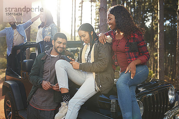 Junge Freunde  die auf einem Jeep mit ihrem Smartphone SMS schreiben und einen Roadtrip genießen