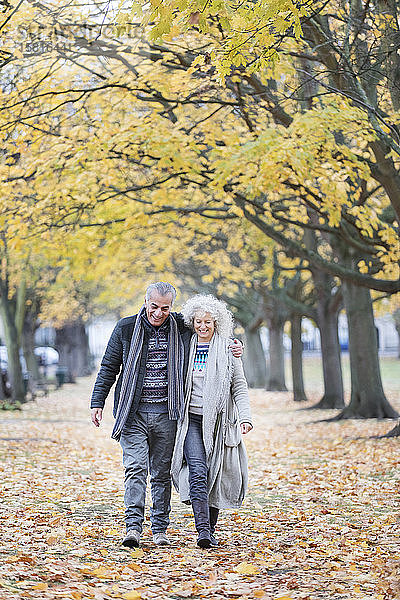 Zärtliches älteres Paar  das zwischen Bäumen und Blättern im Herbstpark spazieren geht