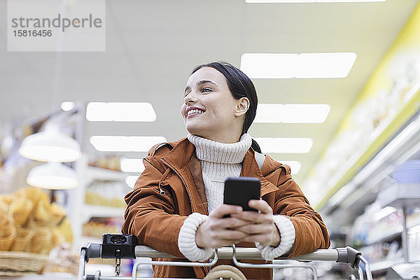 Lächelnde  selbstbewusste Frau mit Smartphone beim Einkaufen im Supermarkt