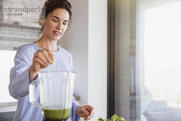 Frau macht gesunden grünen Smoothie im Mixer in der Küche