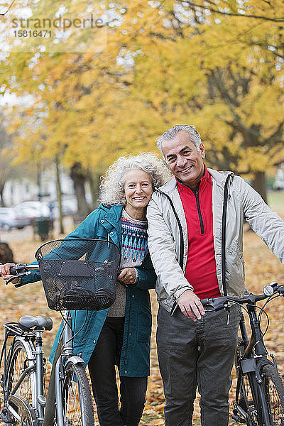 Porträt lächelndes  sorgloses Seniorenpaar mit Fahrrädern im Herbstpark