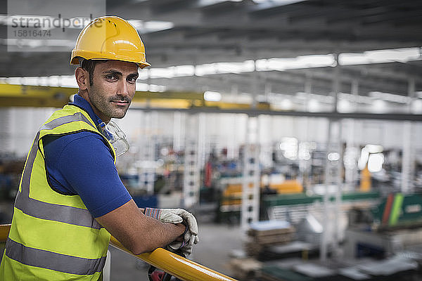 Porträt eines selbstbewussten männlichen Aufsehers  der sich auf ein Geländer in einer Fabrik stützt