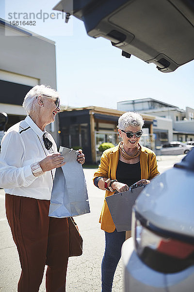 Glückliche Seniorinnen laden Einkaufstüten hinten in einen SUV auf dem Parkplatz eines Einkaufszentrums