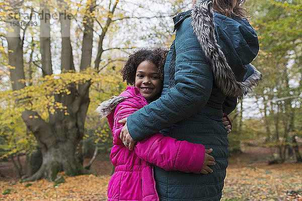 Porträt eines glücklichen Mädchens  das seine Mutter im Herbstwald umarmt