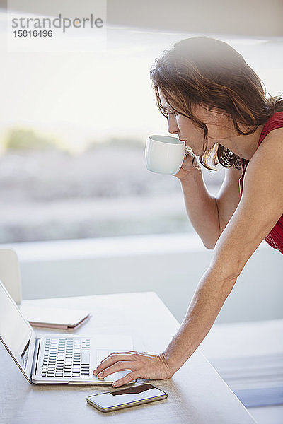 Geschäftsfrau trinkt Kaffee und arbeitet am Laptop
