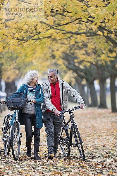 Lächelnde ältere Paar zu Fuß Fahrräder zwischen Bäumen und Blättern im Herbst Park