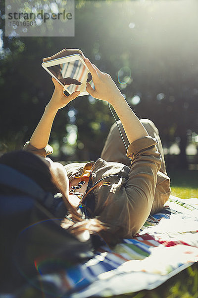 Junge Frau entspannt sich und benutzt ein digitales Tablet in einem sonnigen Sommerpark