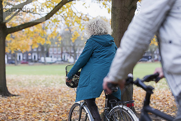 Ältere Frau fährt mit dem Fahrrad zwischen Herbstblättern im Park
