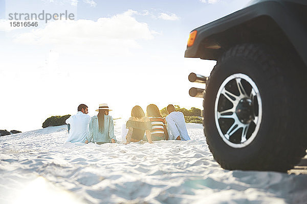 Junge Freunde entspannen sich  hängen am Strand hinter dem Jeep ab