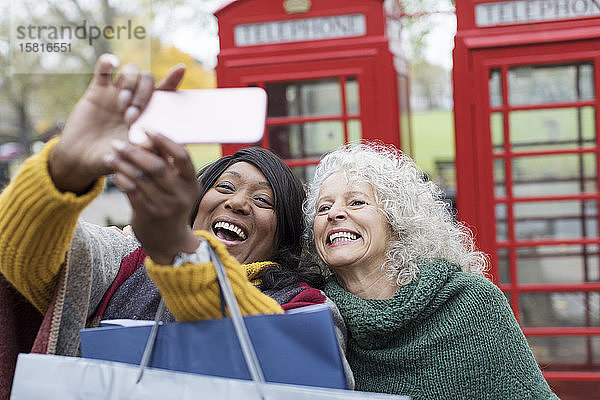 Lächelnde ältere Frauen Freunde nehmen Selfie im Park vor roten Telefonzellen