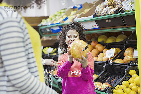 Lächelnde Tochter zeigt der Mutter im Supermarkt eine Grapefruit