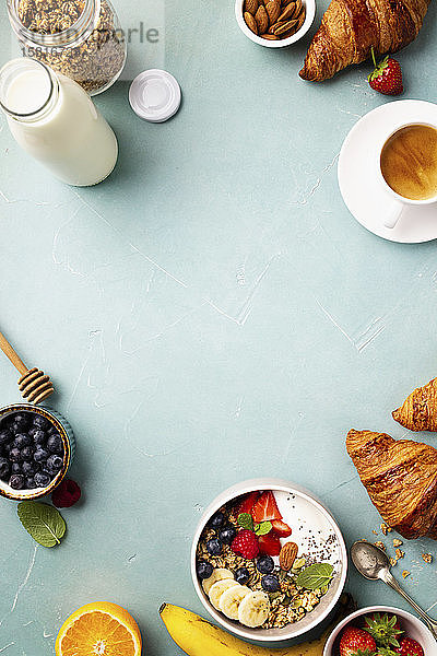 Frühstück mit Müsli  Joghurt  Honig  frischen Bananen  Beeren  Chiasamen in Schale  Kaffee und Croissants