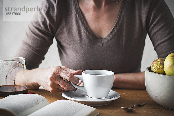 Frauenhand mit einer Kaffeetasse und einem Buch