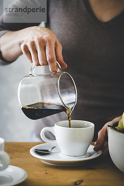 Frauenhand gießt Kaffee in eine Kaffeetasse