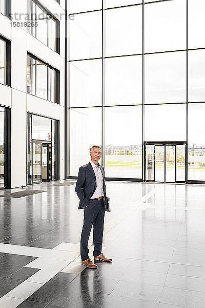 Erfolgreicher Geschäftsmann steht in der Eingangshalle eines Bürogebäudes  mit Händen in den Taschen