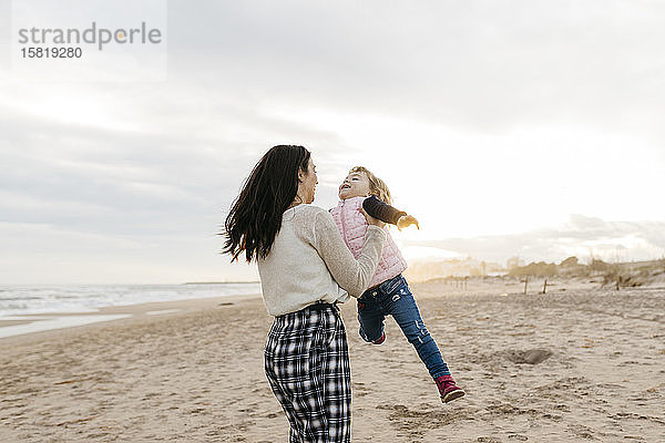 Glückliche Mutter und Tochter spielen bei Sonnenuntergang am Strand