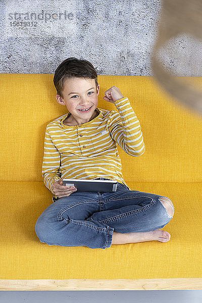 Junge spielt mit Tablette auf gelber Couch