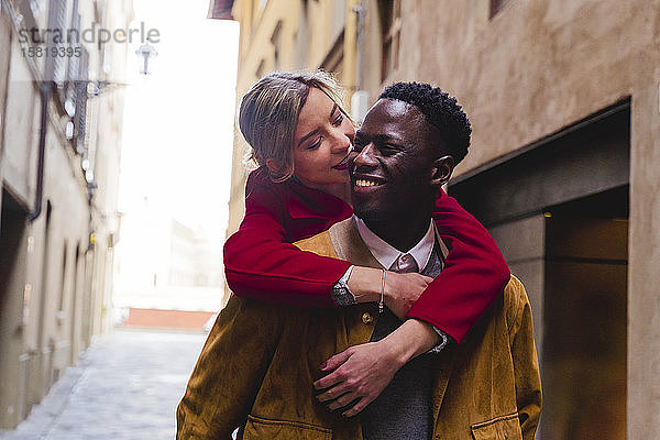 Glücklicher junger Mann trägt seine Freundin huckepack in einer Gasse in der Stadt Florenz  Italien
