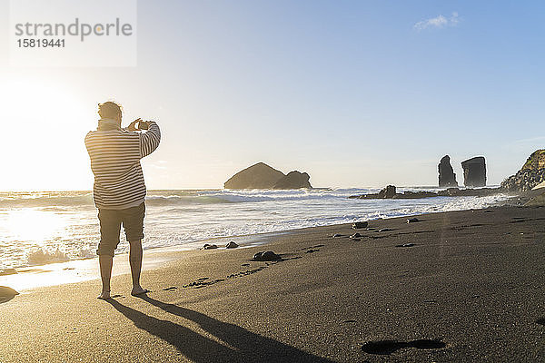 Mann steht bei Sonnenuntergang am Strand und macht Fotos  Sao-Miguel-Insel  Azoren  Portugal