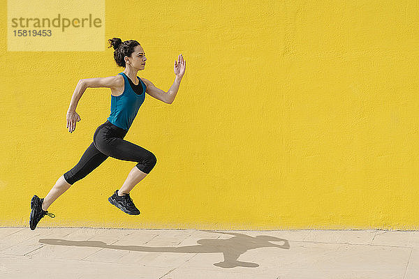 Junge Frau joggt vor einer gelben Wand