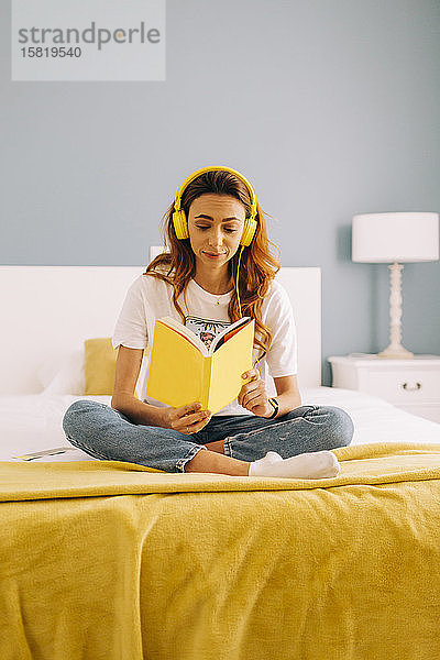 Junge Frau liest ein Buch und hört zu Hause im Bett Musik
