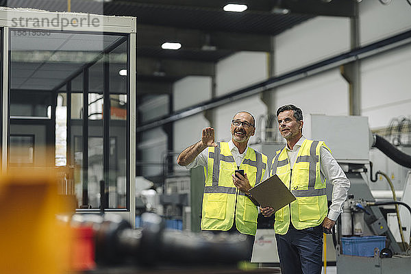 Zwei Männer in reflektierenden Westen sprechen in einer Fabrik