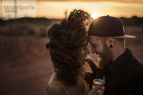 Glückliches Paar trinkt bei Sonnenuntergang im Freien frischen Eistee