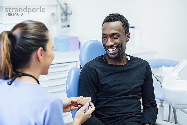 Zahnärztin zeigt lächelnden Patienten Zahnersatz in der medizinischen Praxis