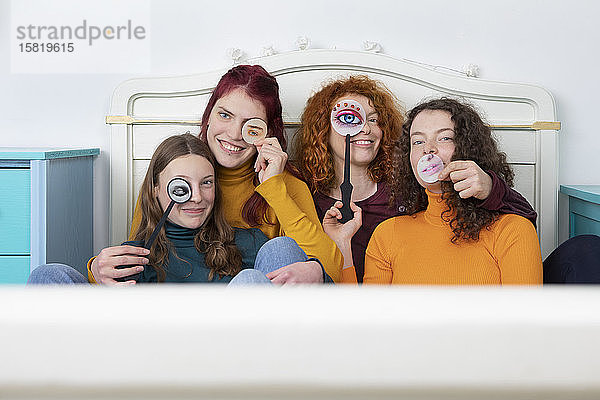 Familienporträt der Mutter und ihrer drei Töchter  die zusammen auf dem Bett sitzen und Papiermasken halten