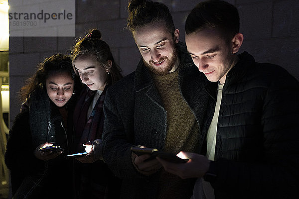 Freunde betrachten beleuchtete Smartphones im Dunkeln