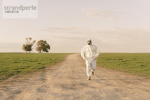 Mann mit Schutzanzug und Maske läuft auf Feldwegen auf dem Land