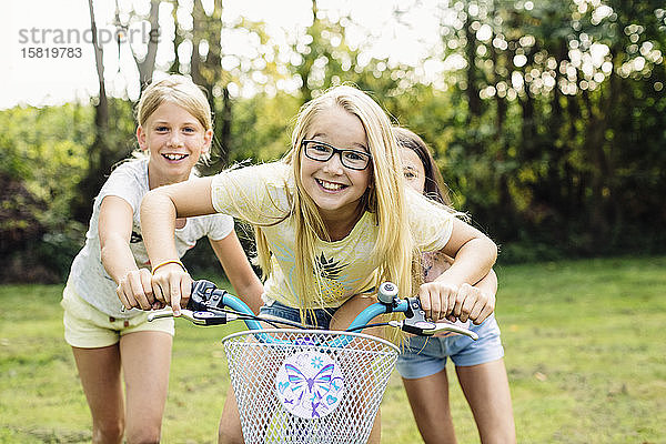 Glückliche Mädchen fahren Fahrrad im Garten