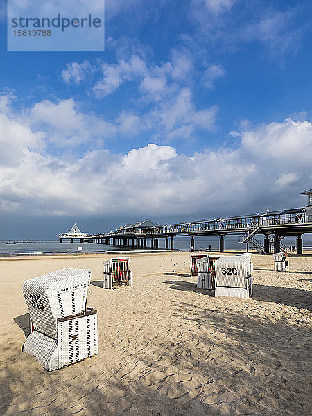 Deutschland  Mecklenburg-Vorpommern  Heringsdorf  Wolken über Kapuzenstrandkörben am sandigen Küstenstrand mit Pier im Hintergrund