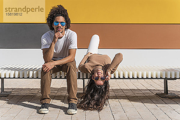 Paar mit Sonnenbrille  entspannt auf der Bank  ein Partner auf dem Rücken liegend mit herabhängendem Kopf