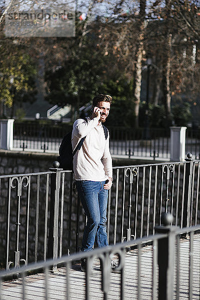 Lächelnder Mann auf einer Brücke beim Telefonieren