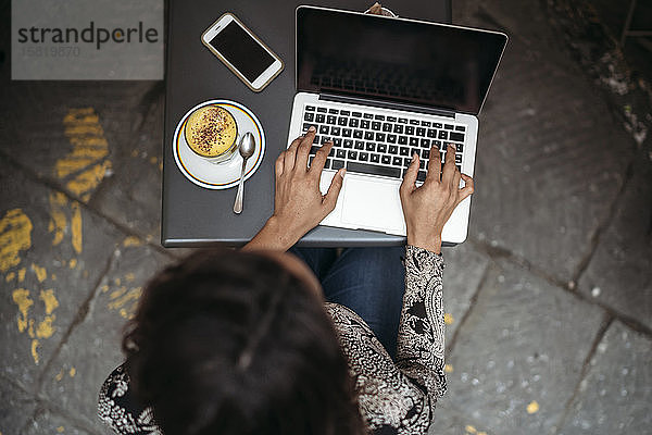 Draufsicht einer jungen Frau mit Laptop in einem Straßencafé