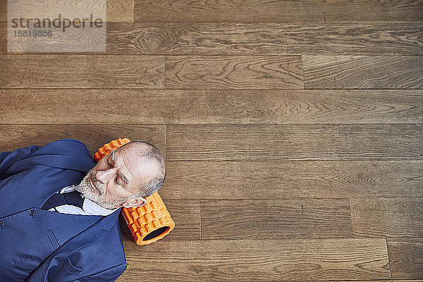Älterer Geschäftsmann entspannt sich auf Holzboden  ruht auf Faszienrolle