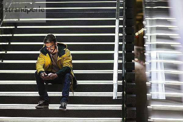 Lächelnder Mann sitzt auf der Treppe in der U-Bahn-Station und benutzt sein Handy